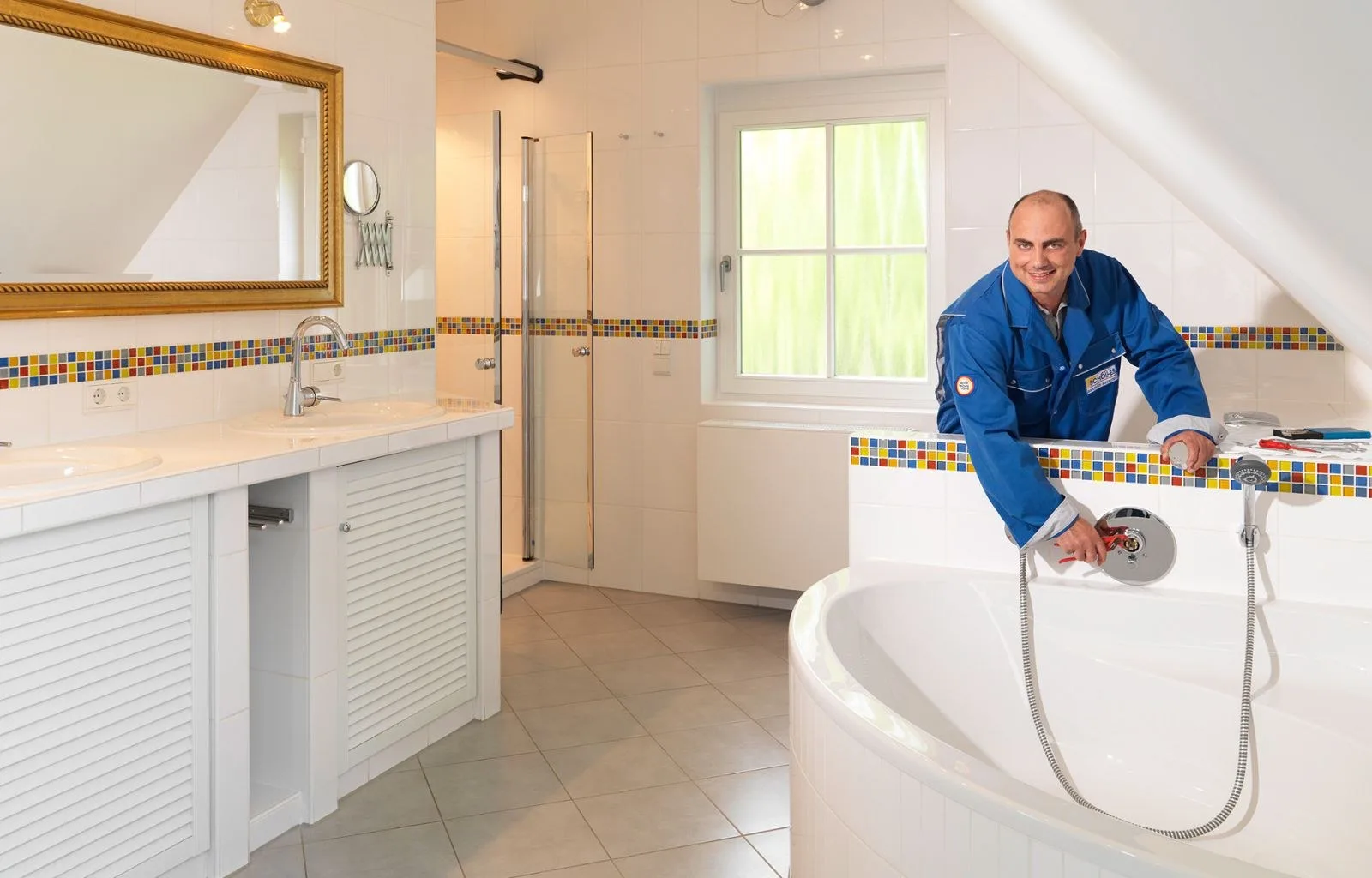 Monteur in blauer Schölles-Arbeitskleidung montiert die Armatur einer Badewanne in einem hellen Bad