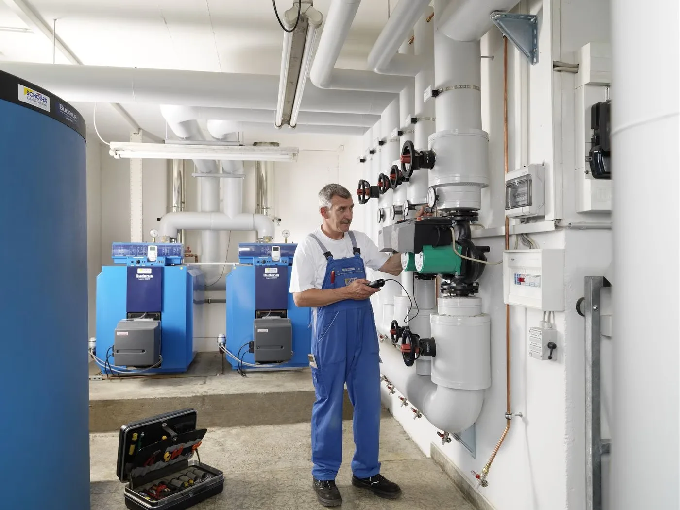 Monteur in blauer Latzhose mit Schölles-Aufnäher prüft eine Pumpengruppe in einer Heizzentrale