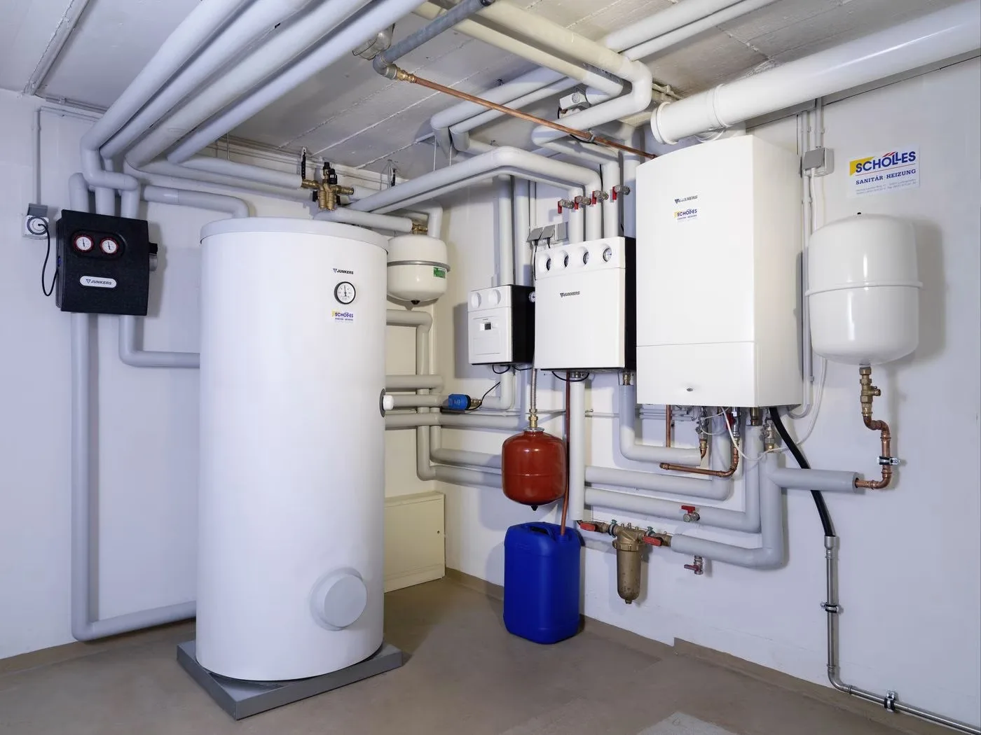 Heizraum mit Warmwasserspeicher, Wandgeräten, Ausdehnungsgefäß und Schölles-Schild an der Wand